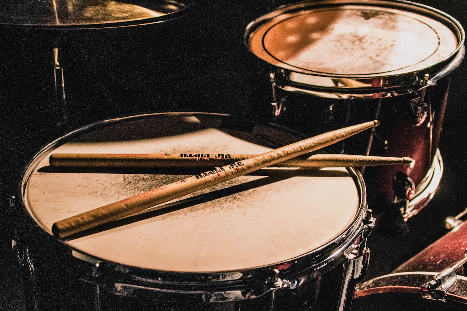 Crossed drumsticks on a snare beside rack toms